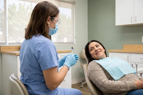 Hygienist in a mask and gloves chatting with a smiling patient in the dental chair