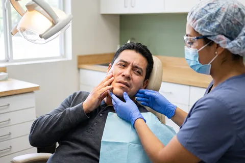 Man with a toothache holding his cheek while the dentist gently checks his jaw