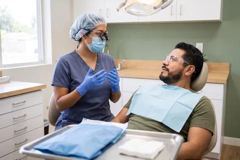 Man in safety glasses listening to a dentist in loupes, with a sealed sterile pack on the tray