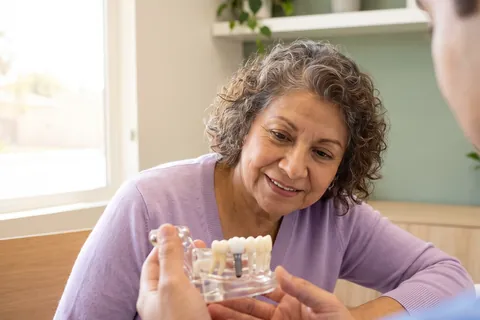 Older woman looking at a dental implant model her dentist is holding